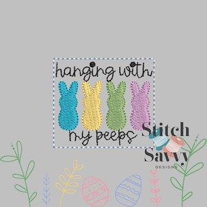 Peut inclure: Une broderie avec quatre lapins colorés en bleu, jaune, vert et violet, avec le texte "hanging with my peeps". Le motif est posé sur un fond gris, avec des graphiques supplémentaires sur le thème de Pâques.