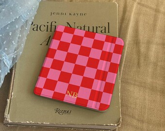 May include: A red and pink chequered phone case with the initials "NB" rests on a book titled "Pacific Natural" by Jenni Kayne. The book is a light green colour and has the Rizzoli logo on the bottom.