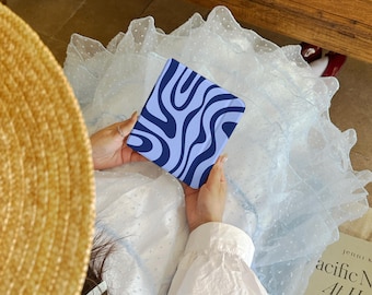 May include: A square e-reader device featuring a light blue and dark blue wavy, abstract zebra-like pattern on its front cover. The device is held in a neutral position, displaying a smooth, matte finish across its surface with curved edges.