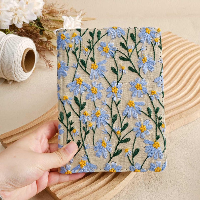 Pode incluir: Uma pequena bolsa de linho bege com fecho de correr, bordada com um padr&atilde;o floral de flores azuis e amarelas.
