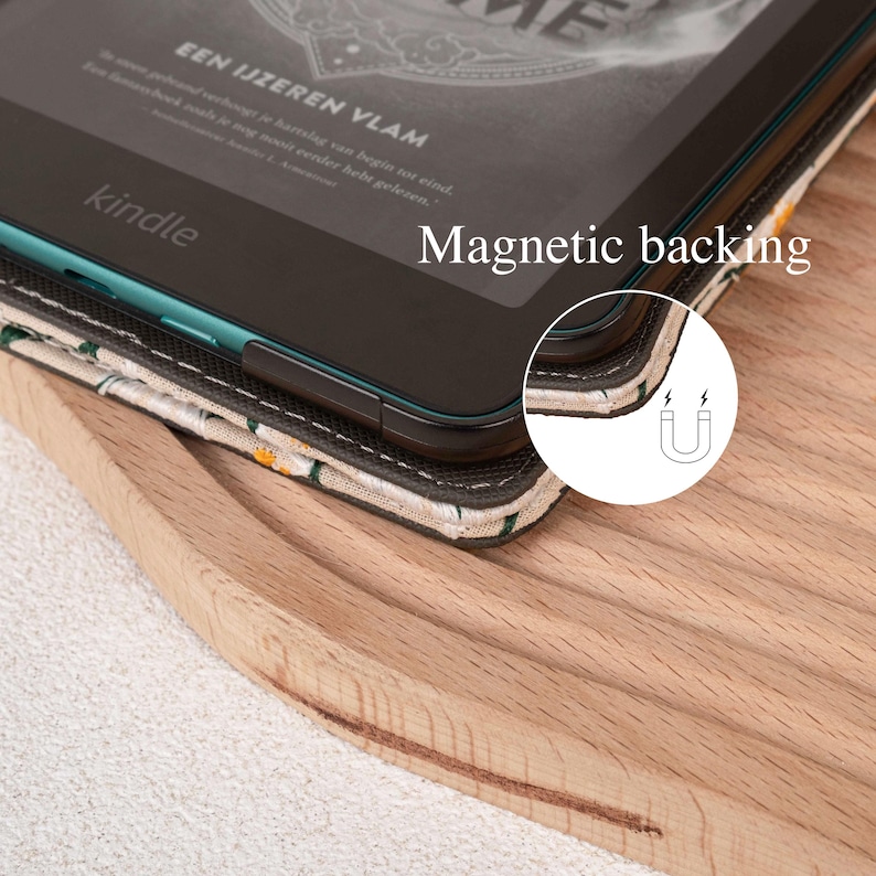 Pode incluir: Um leitor de e-books preto com uma borda verde e a palavra "kindle" na frente. O leitor de e-books est&aacute; em uma capa de tecido bege com um padr&atilde;o floral. A capa tem um fecho magn&eacute;tico, indicado por um s&iacute;mbolo de &iacute;m&atilde;.