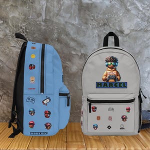 Pode incluir: Duas mochilas, uma azul clara e outra cinza, com designs tem&aacute;ticos do jogo Roblox. A mochila azul tem v&aacute;rios &iacute;cones relacionados ao jogo e o logotipo da Roblox. A mochila cinza exibe um personagem segurando um controle de jogo, com o nome "MARCEL" abaixo.