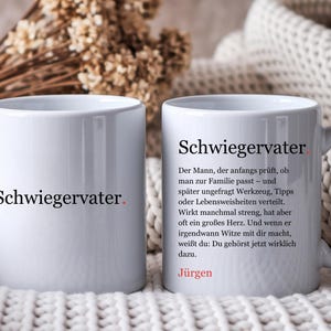 Könnte beinhalten: Zwei weiße Keramiktassen mit schwarzem Text. Die linke Tasse zeigt das Wort Schwiegervater mit einem roten Punkt. Die rechte Tasse zeigt das Wort Schwiegervater, gefolgt von einer deutschen Definition und dem Namen Jürgen in roter Schrift.