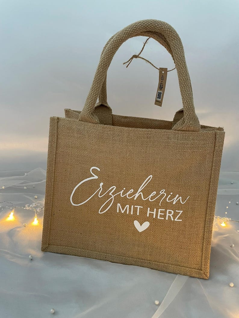 May include: A brown burlap tote bag with white text that reads "Erzieherin mit Herz" and a white heart.