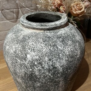 May include: A large, round, grey ceramic vase with a white speckled finish. The vase is sitting on a wooden surface.