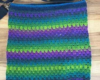 May include: A crocheted shoulder bag with a black adjustable strap. The bag is made with a multi-colored yarn in shades of green, purple, and blue.