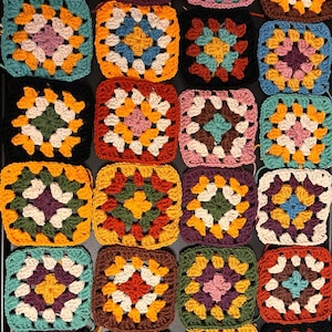 May include: A collection of colorful crocheted granny squares in various colors, including red, orange, yellow, green, blue, purple, brown, and white.