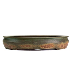 May include: A low, oval-shaped ceramic bonsai pot featuring a textured exterior with a mottled finish in shades of earthy brown, muted green, and rust orange. The rim is slightly raised and defined, with a smooth, dark interior basin visible.