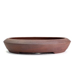 May include: A shallow, oval-shaped bonsai pot with a textured, dark reddish-brown finish. The container features a wide, angled rim and a low profile, supported by small, integrated feet at the base, presenting a simple and functional design.