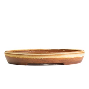 May include: An oval-shaped ceramic bonsai pot with a low profile and a wide, shallow basin. The exterior features a matte, earthy brown finish on the lower section, transitioning to a smooth, creamy beige glaze along the upper rim and interior.