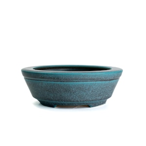 May include: A teal-colored ceramic bonsai pot with a textured surface. The oval-shaped pot has a wide opening and a slightly flared base. The pot is designed with a simple, yet elegant aesthetic.