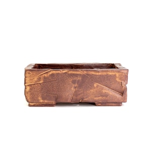May include: A rectangular, brown ceramic planter with a textured, geometric design. The planter has a rough, weathered appearance and is suitable for small plants or succulents. The planter is approximately 10 inches long, 5 inches wide, and 4 inches tall.