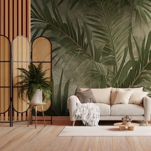 K&ouml;nnte beinhalten: Ein Wohnzimmer mit einem wei&szlig;en Sofa, einem geflochtenen Paravent und einer Tapete mit tropischen Bl&auml;ttern. Das Sofa hat eine Wolldecke und Kissen. Es gibt einen kleinen Tisch mit einer Topfpflanze und einen Beistelltisch mit einer Vase mit Blumen.
