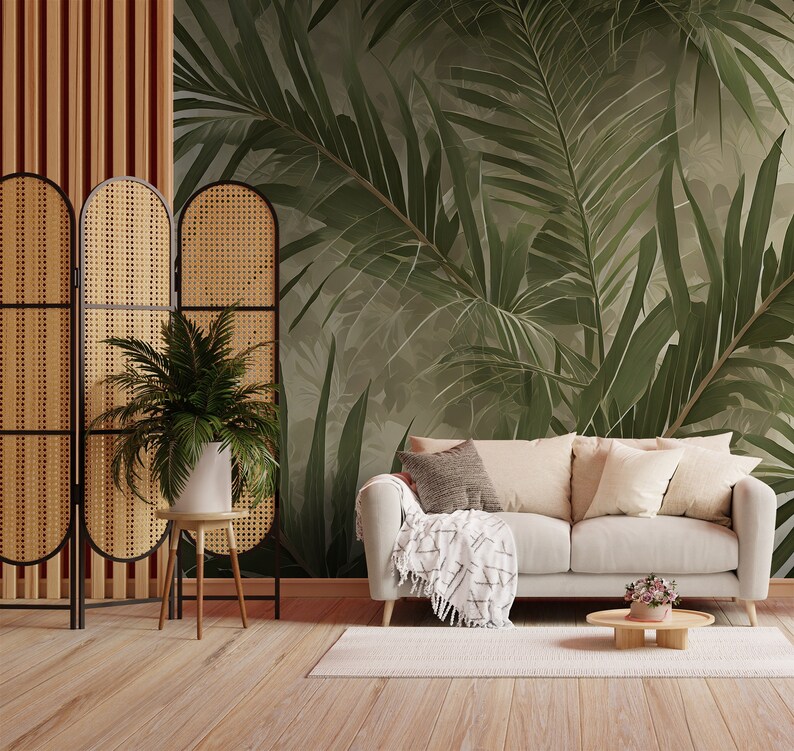 K&ouml;nnte beinhalten: Ein Wohnzimmer mit einem wei&szlig;en Sofa, einem geflochtenen Paravent und einer Tapete mit tropischen Bl&auml;ttern. Das Sofa hat eine Wolldecke und Kissen. Es gibt einen kleinen Tisch mit einer Topfpflanze und einen Beistelltisch mit einer Vase mit Blumen.