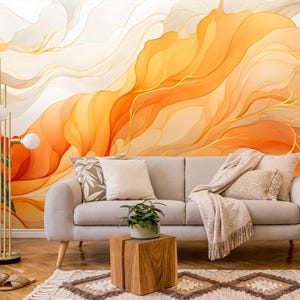 Può includere: Un soggiorno con un divano grigio chiaro, cuscini e una coperta. La parete presenta un murale astratto nei toni dell'arancione, giallo e bianco. Una lampada da terra dorata e piante in vaso completano l'arredamento.