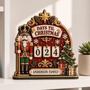 Könnte beinhalten: Ein hölzerner Weihnachts-Countdown-Kalender mit einer Nussknacker-Figur, einem geschmückten Baum und drei Nummernkarten, die 024 anzeigen. Das Schild trägt die Aufschrift DAYS TIL CHRISTMAS und ANDERSON FAMILY in dunkler Schrift.