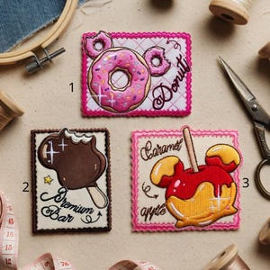 May include: Three embroidered patches with food designs: a pink donut with the word "Donut", a chocolate ice cream bar with "Premium Bar", and a caramel apple with "Caramel apple". Sewing supplies are scattered around.