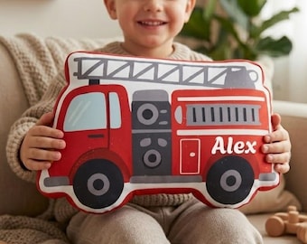 May include: A plush throw pillow shaped like a red fire truck with a white ladder on top, black wheels, and the name Alex printed in white script on the side. The pillow features a detailed graphic design of a fire engine with grey accents.