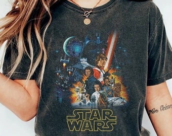 Könnte beinhalten: Ein schwarzes Vintage-T-Shirt mit einem verblassten Grafikdruck von Figuren aus dem Star Wars-Film-Franchise. Die Grafik zeigt Darth Vader, Luke Skywalker, Prinzessin Leia, Han Solo, Chewbacca und Yoda. Der Text "STAR WARS" ist in Gelb unter der Grafik gedruckt.