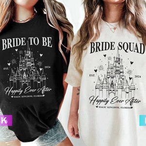 K&ouml;nnte beinhalten: Zwei T-Shirts mit einer wei&szlig;en Umrandung von Cinderellas Schloss, Text, der "Bride to Be" und "Bride Squad" sagt, und dem Text "Happily Ever After" mit den Worten "Magic Kingdom, Florida" darunter. Das Shirt auf der linken Seite ist schwarz und das Shirt auf der rechten Seite ist elfenbein.