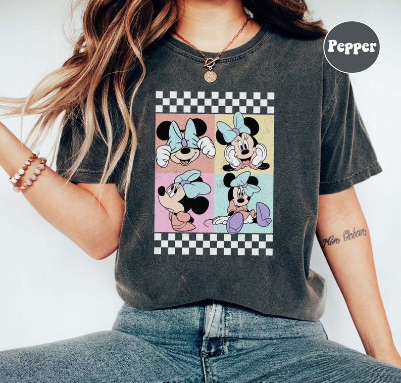 May include: A dark grey t-shirt with a chequered pattern and a graphic of four different images of Minnie Mouse. The graphic is in a retro style with pastel colours.