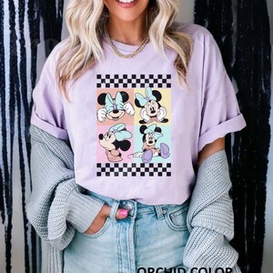 May include: A light purple t-shirt featuring a graphic of four cartoon images of Minnie Mouse in a checkered pattern. The text "ORCHID COLOR" is printed at the bottom of the image.
