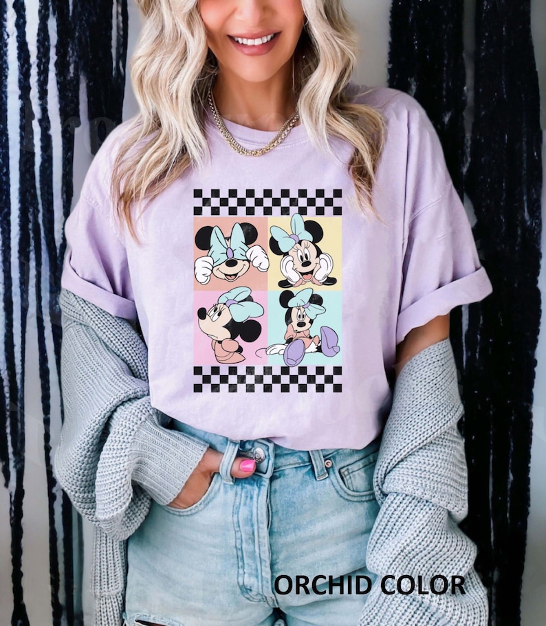 May include: A light purple t-shirt featuring a graphic of four cartoon images of Minnie Mouse in a checkered pattern. The text "ORCHID COLOR" is printed at the bottom of the image.