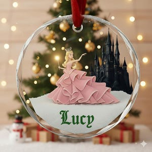 以下が含まれることがあります： プリンセスデザインの透明なファセットクリスマスオーナメント。オーナメントは、ピンクのガウンを着たプリンセス、魔法の杖、黒い城、緑色のスクリプトで「Lucy」という名前が特徴です。吊り下げ用の赤いリボンが付いています。