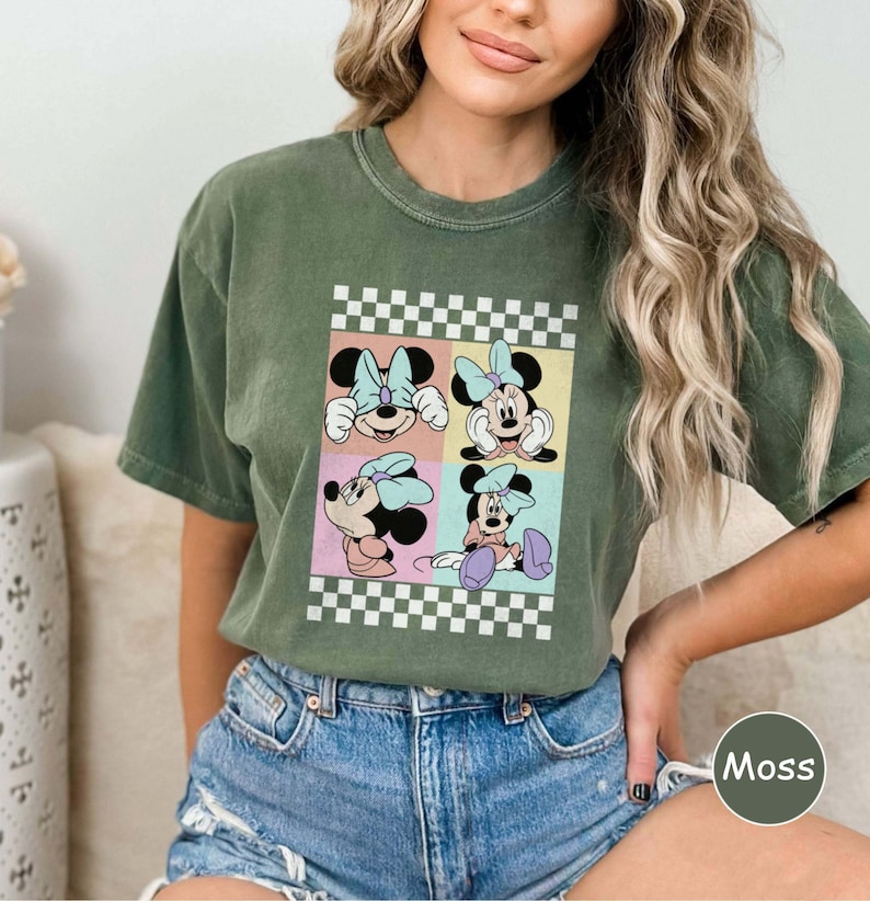May include: A green t-shirt featuring a vintage-style graphic of Minnie Mouse in four different poses. The graphic is surrounded by a checkered border.