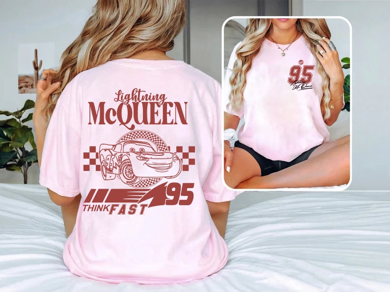 May include: Pink t-shirt featuring a red graphic of Lightning McQueen from the Cars film. The graphic includes the text "Lightning McQueen", "Think Fast", and "95".