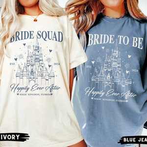 K&ouml;nnte beinhalten: Zwei T-Shirts mit einer wei&szlig;en Umrandung von Cinderellas Schloss, Feuerwerk und Mickey-Maus-Ohren. Der Text auf dem elfenbeinfarbenen Shirt lautet "Bride Squad Est. 2024 Happily Ever After Magic Kingdom, Florida". Der Text auf dem Jeans-Shirt lautet "Bride to Be Est. 2024 Happily Ever After Magic Kingdom, Florida".