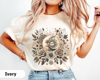 Op de afbeelding: Een wit T-shirt met een grafische print van een zon en maan met bloemdetails. De zon en maan zijn gestileerd en hebben een vintage esthetiek. De bloemen zijn in tinten bruin en beige.