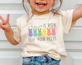 Puede incluir: Una camiseta blanca con un gráfico de coloridos Peeps de Pascua y el texto "Jesús ha resucitado, dilo a tus peeps".