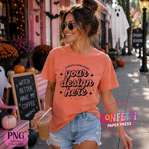 May include: A coral-colored short-sleeve t-shirt featuring black text that reads "CONFETTI PAPER PRESS" in a circular arc above the words "your design here" in a bold, wavy font, accented by small four-pointed star icons.