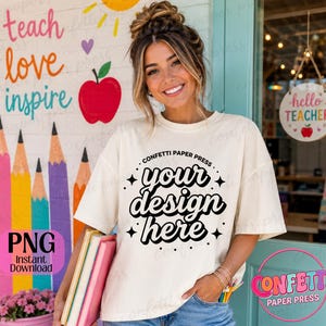 Op de afbeelding: Een off-white t-shirt met korte mouwen voorzien van de zwarte tekst "CONFETTI PAPER PRESS" in een cirkelvormige boog boven de woorden "your design here" in een vet, golvend lettertype, geaccentueerd door kleine zwarte sterpictogrammen.