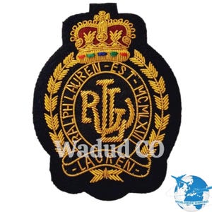 Op de afbeelding: Een zwart geborduurd embleem met een gouden kroon en laurierkrans ontwerp. Het embleem bevat de tekst "RALPH LAUREN" en de initialen "RL" in gouddraad. Het embleem heeft een decoratieve vorm en is geschikt voor kleding.