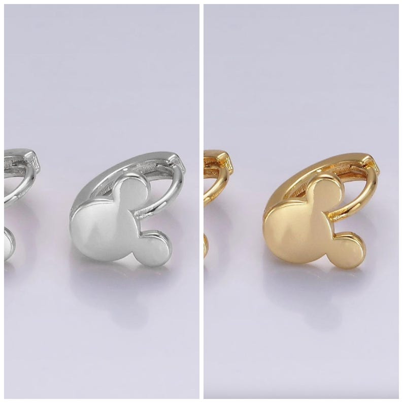 Op de afbeelding: Zilveren en goudkleurige Mickey Mouse-vormige oorringen. De oorbellen hebben een gladde, gepolijste afwerking en een klassiek ontwerp. De oorbellen worden op een lichte achtergrond getoond.