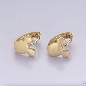 Op de afbeelding: Een paar goudkleurige oorringen. Elke oorring heeft een Mickey Mouse-hoofdontwerp. De oorbellen zijn gemaakt van een glanzend, metallic materiaal en staan tegen een lichte achtergrond.
