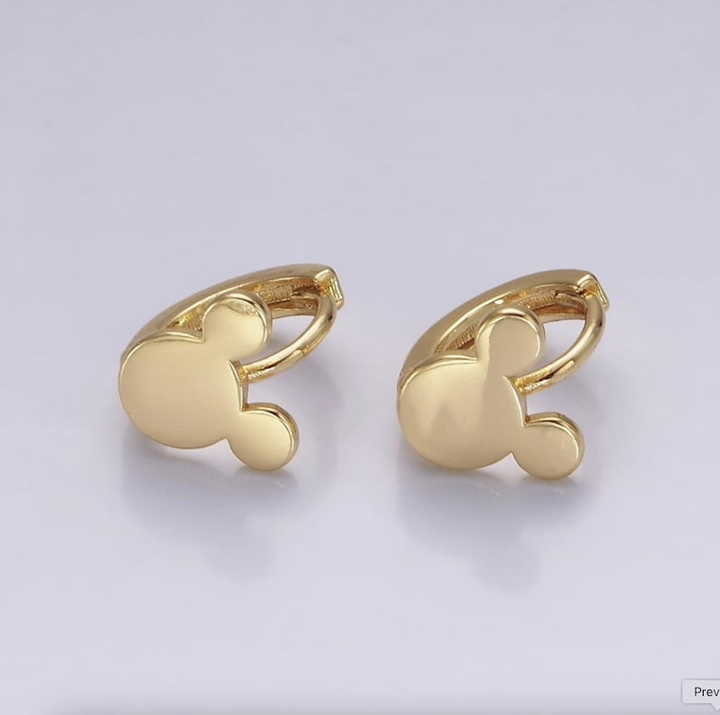 Op de afbeelding: Een paar goudkleurige oorringen. Elke oorring heeft een Mickey Mouse-hoofdontwerp. De oorbellen zijn gemaakt van een glanzend, metallic materiaal en staan tegen een lichte achtergrond.