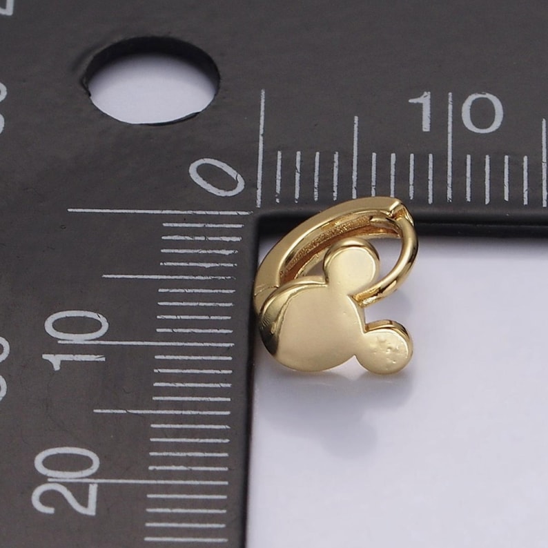 Op de afbeelding: Een goudkleurige oorbel met een Mickey Mouse-hoofdontwerp. De oorbel is een kleine oorring, met het iconische muissilhouet als belangrijkste bedel. De oorbel wordt naast een liniaal getoond voor de schaal.