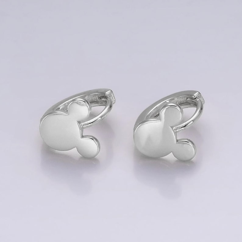 Op de afbeelding: Een paar zilverkleurige oorringen, elk in de vorm van een Mickey Mouse-hoofd. De oorbellen hebben een gladde, gepolijste afwerking en een eenvoudig ontwerp. Ze worden gepresenteerd tegen een lichte achtergrond.