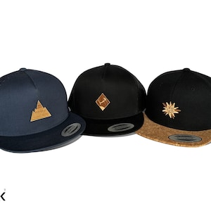 Può includere: Tre cappellini da baseball con diversi design. Uno è blu navy con un design a montagna, un altro è nero con un design a diamante e il terzo è nero con un design a fiore. Tutti hanno una visiera curva.
