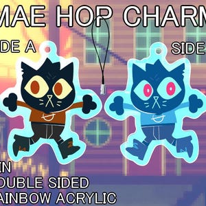 May include: Double-sided 5 cm rainbow acrylic charm featuring a cartoon cat character. Side A has a brown shirt and side B has a blue shirt. The charm has a black lanyard attached. Text on the charm reads "MAE HOP CHARM", "SIDE A", "SIDE B", and "2 IN DOUBLE SIDED RAINBOW ACRYLIC".