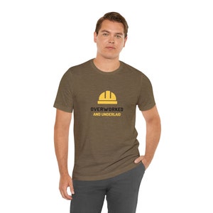 May include: A brown t-shirt with a yellow hard hat graphic and the text "Overworked and Underlaid".