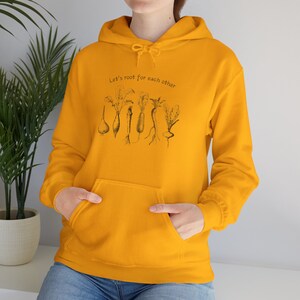Könnte beinhalten: Ein gelber Hoodie mit einer schwarzen Grafik verschiedener Wurzelgemüse und dem Text "Let's root for each other".