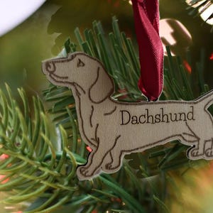 May include: A wooden Christmas ornament shaped like a dachshund dog. The ornament is painted brown and has the word "Dachshund" written on it.