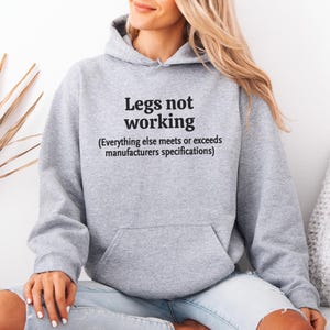 Sudadera con capucha unisex para adultos con texto "Piernas que no funcionan" y humor para concientizar sobre la discapacidad. Usuario de silla de ruedas.