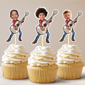 Könnte beinhalten: Drei Cupcakes, verziert mit weißem Frosting und gekrönt mit Gitarre spielenden Cartoon-Figuren. Die Figuren tragen alle rote Hemden und blaue Jeans. Die Gitarren sind mit weißen und goldenen Details verziert.