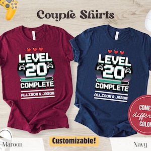 May include: Maroon and navy blue couple shirts with a video game theme. Each shirt features the text "Level 20 Complete" with a pixelated design and the names "Allison & Jason". The shirts are customizable and come in different colours.