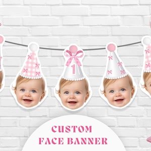 May include: A personalised banner with smiling baby faces wearing party hats. The hats are white with pink details, some with gingham patterns and bows. Pink balloons and a star-shaped balloon are also visible.